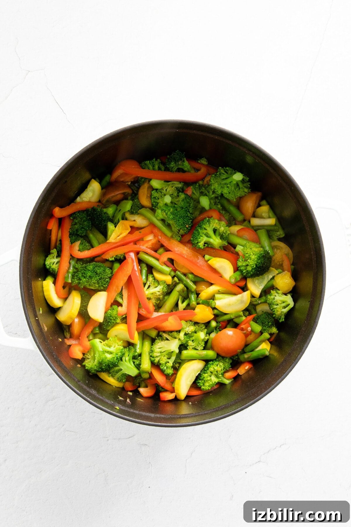A white surface with a pan of pasta primavera containing vegetables.
