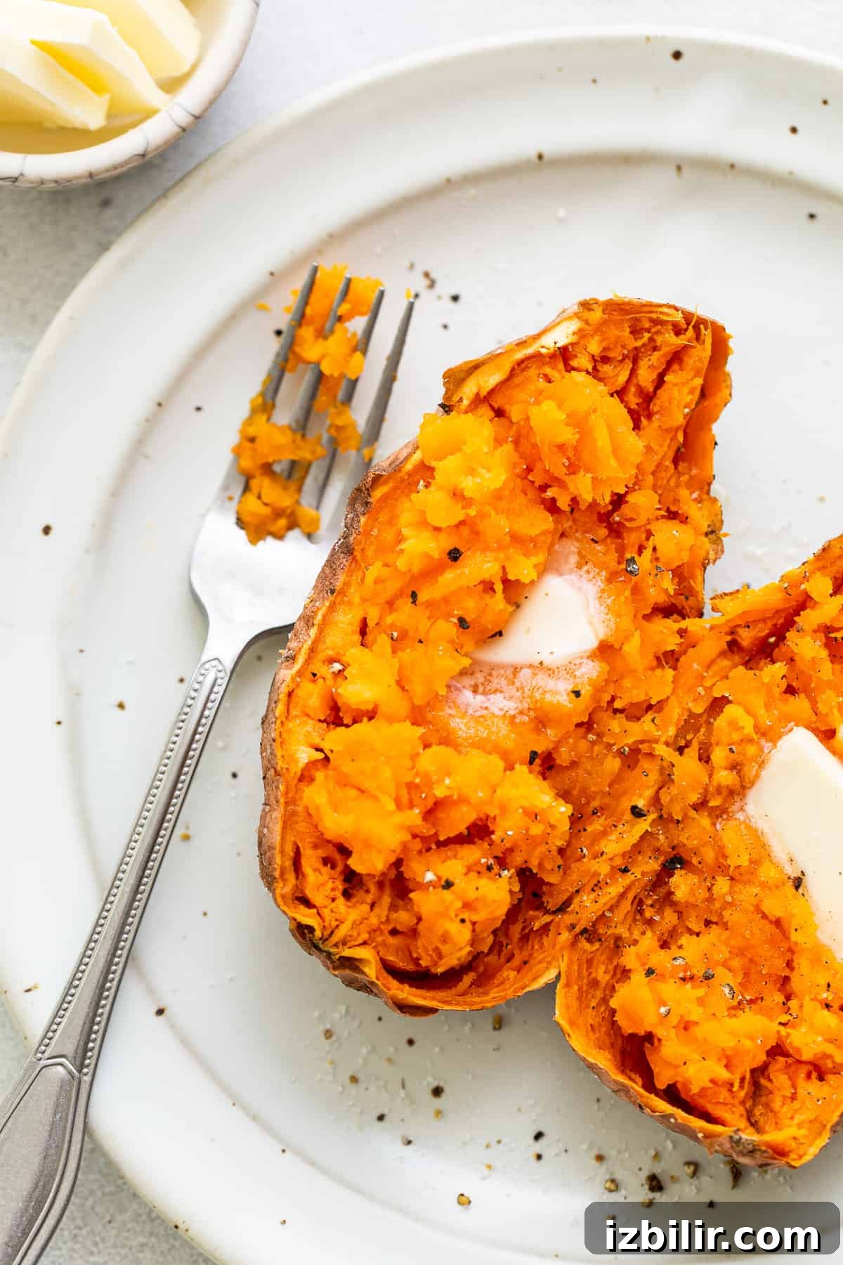 Microwave Sweet Potato to Tender Perfection 2 A cooked sweet potato on a plate with butter and pepper.
