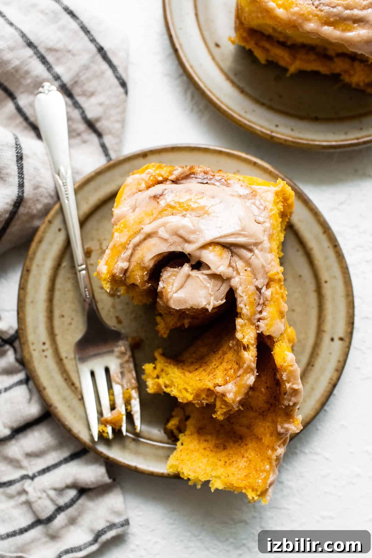 These pumpkin cinnamon rolls are topped with a yummy cinnamon cream cheese frosting! We’re also sharing how to prepare them the night before and bake in the morning. Pumpkin cinnamon roll on a plate with a fork.