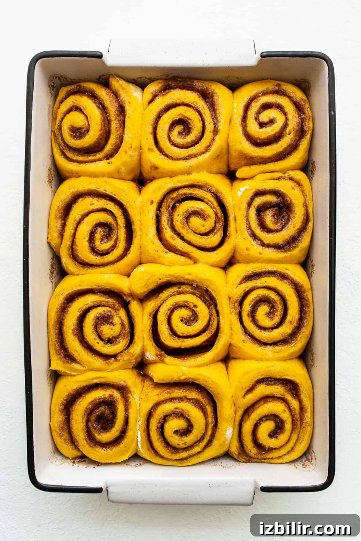 Fluffy Pumpkin Cinnamon Rolls with Cream Cheese Glaze 3 Pumpkin cinnamon rolls in a baking dish.