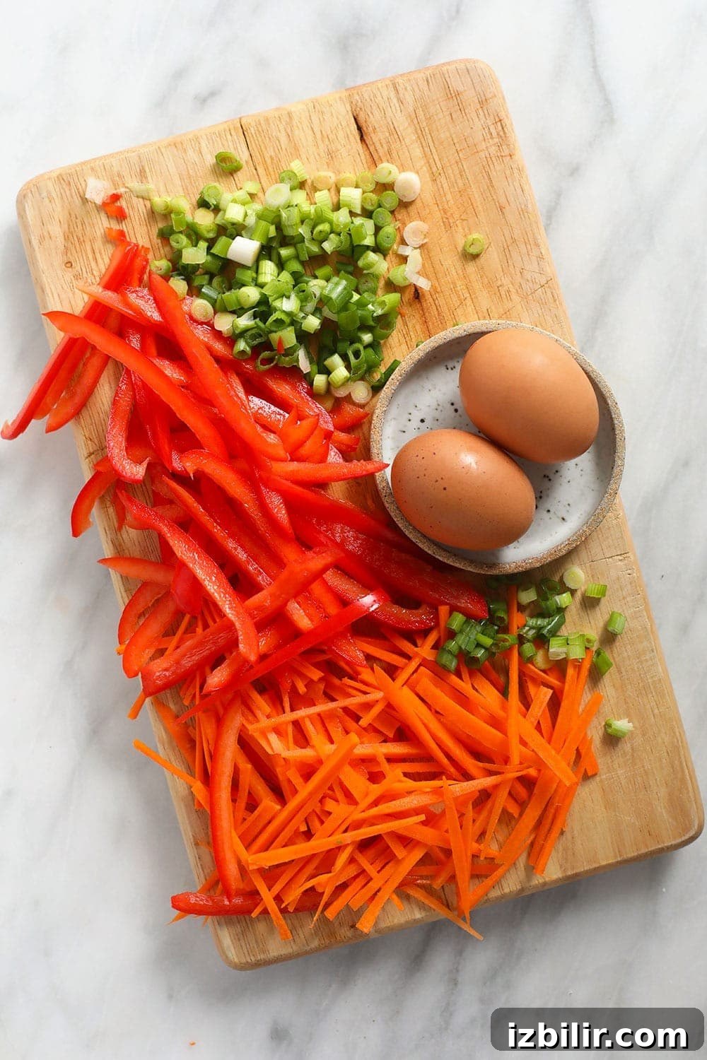 Green onion, red pepper, eggs, and carrots on a cutting board.