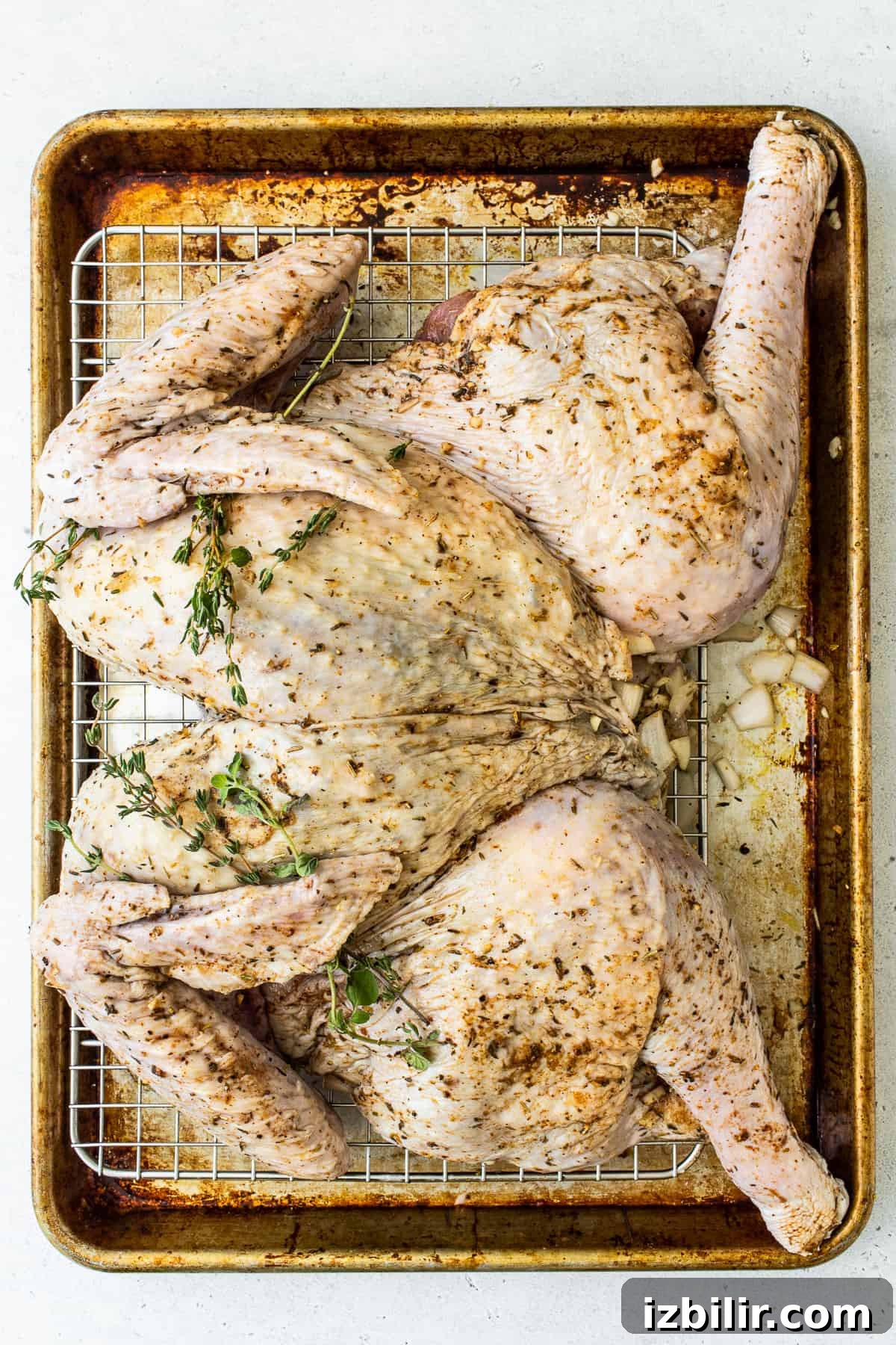 Spatchcocked turkey on a baking sheet with fresh herbs.
