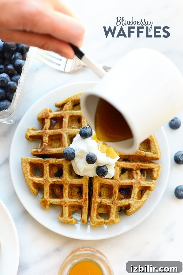 Syrup being poured on a blueberry waffle