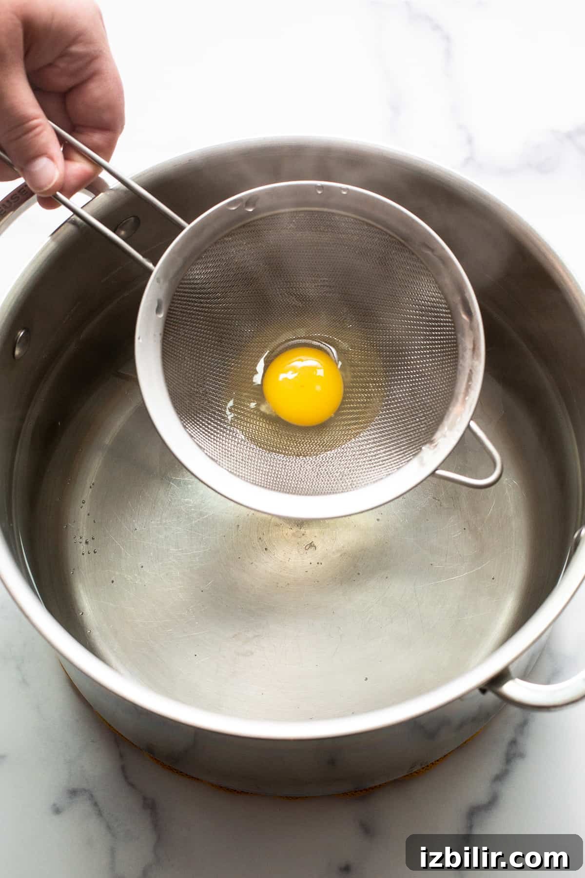 Placing egg strainer into simmering water Raw egg in a strainer being set in a pot of boiling water.