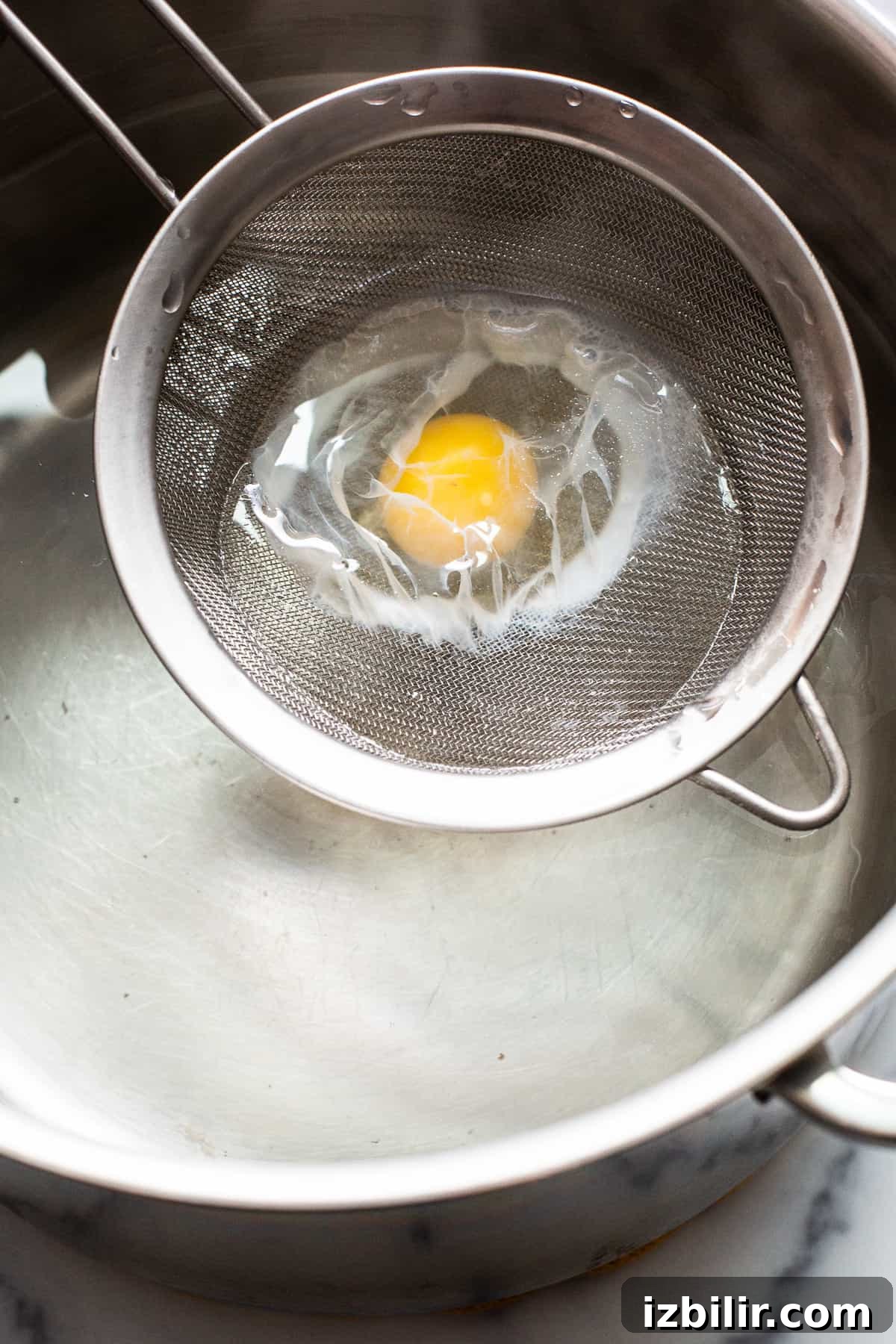 Egg in strainer Raw egg in a mesh strainer being put in a pot of boiling water.