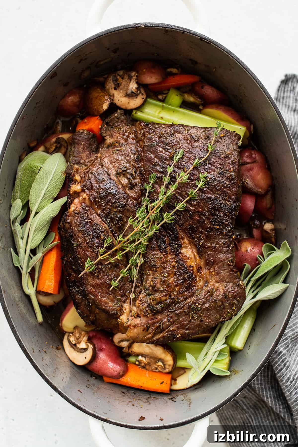 Finished pot roast with fresh herbs and gravy. Pot roast in a dutch oven topped with fresh herbs.