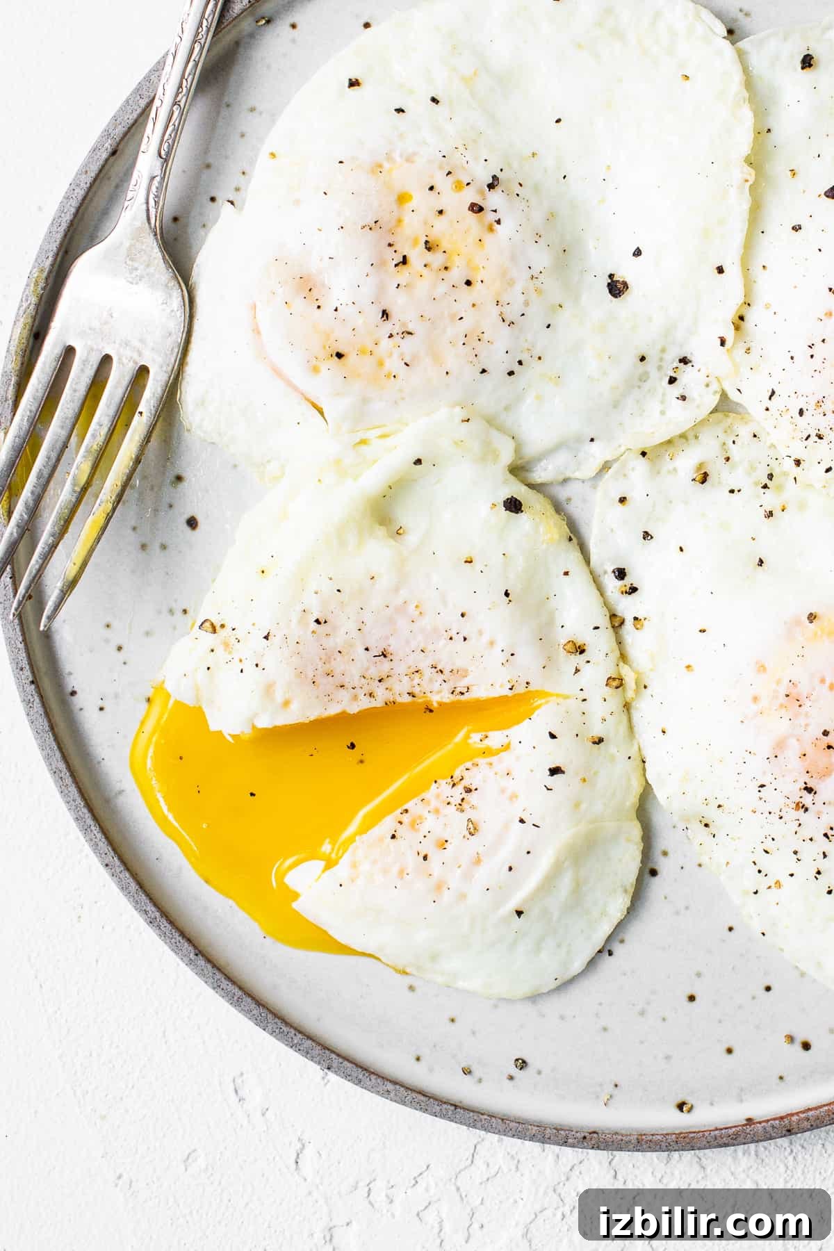 This over easy eggs recipe uses a simple technique that creates the perfect runny yolk and fluffy egg whites every time. Over easy eggs on a plate with a fork.