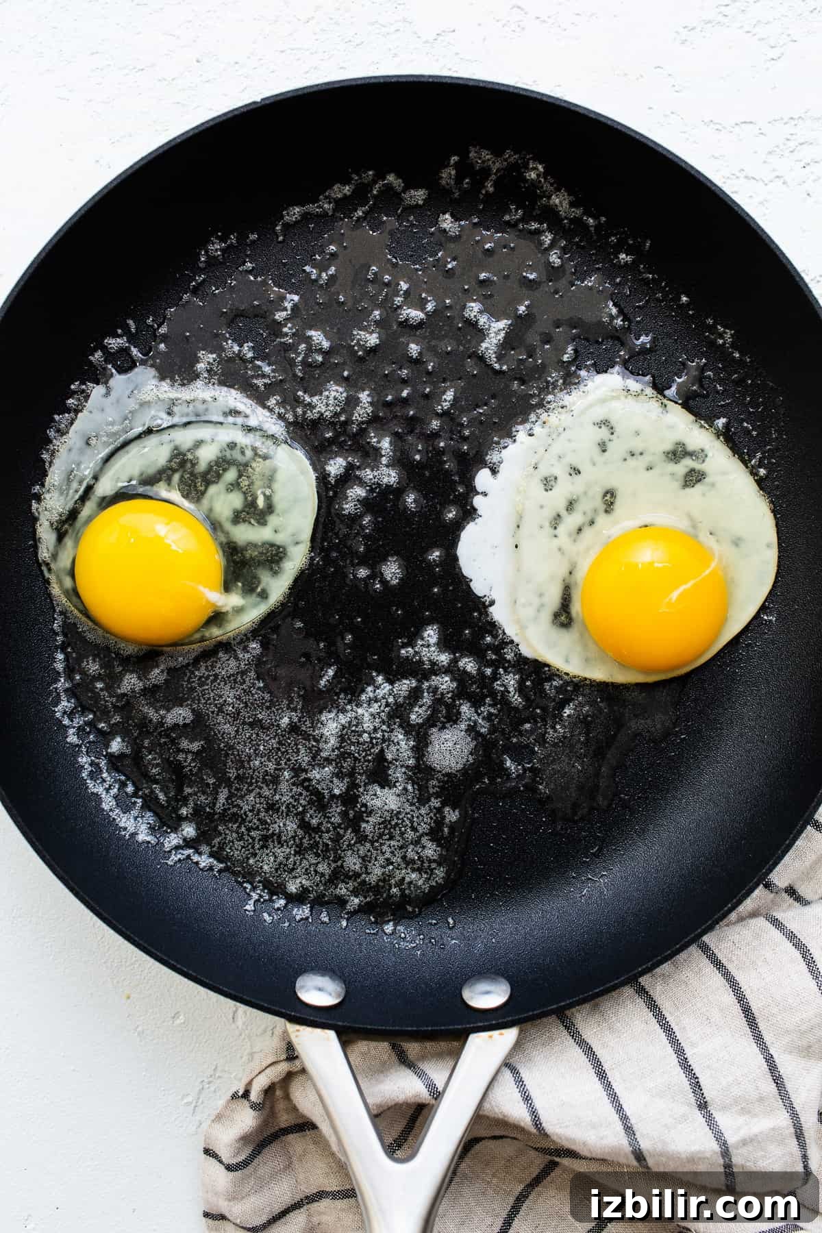 This over easy eggs recipe uses a simple technique that creates the perfect runny yolk and fluffy egg whites every time. Eggs cooking in a skillet.