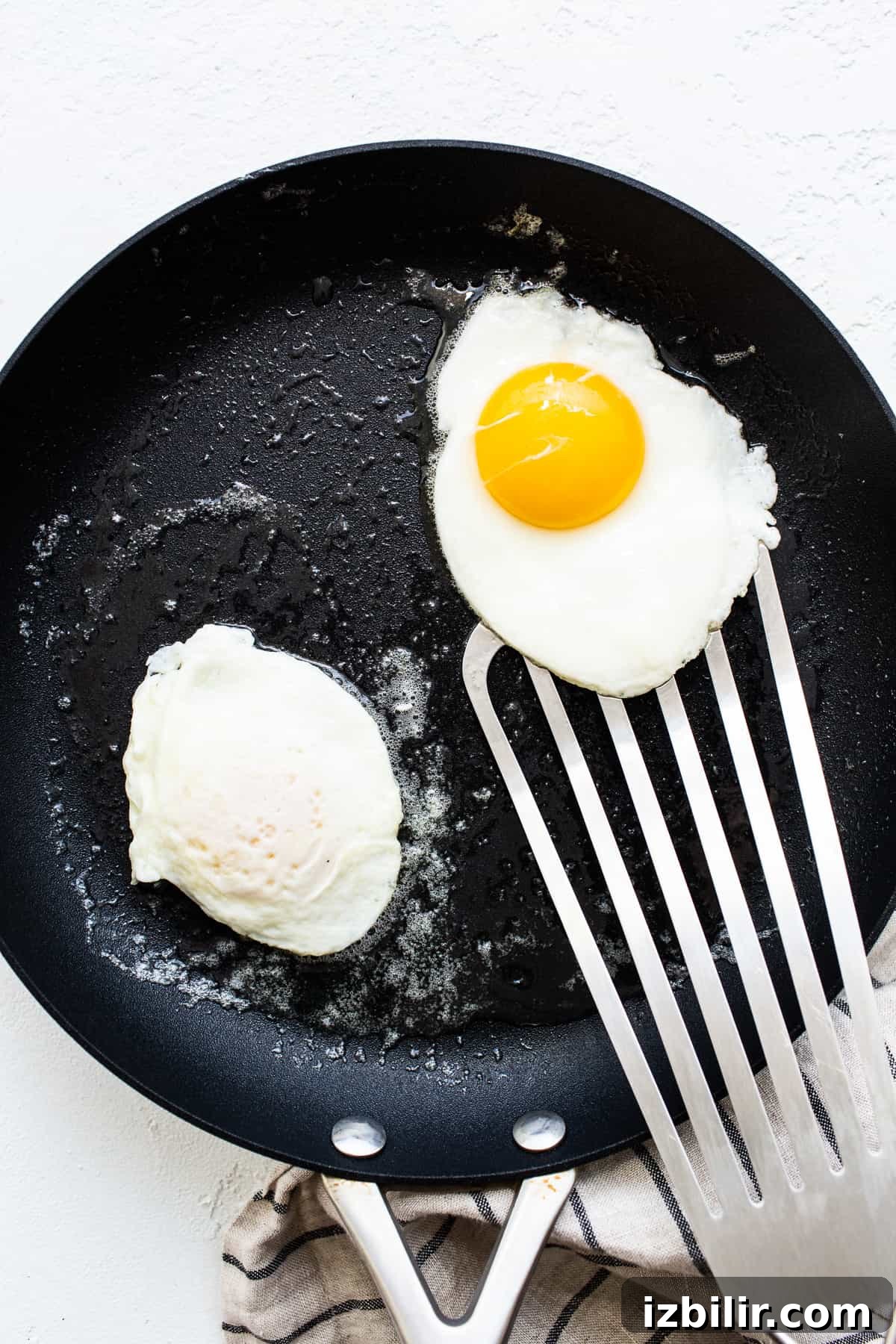 This over easy eggs recipe uses a simple technique that creates the perfect runny yolk and fluffy egg whites every time. Eggs cooking in a skillet.