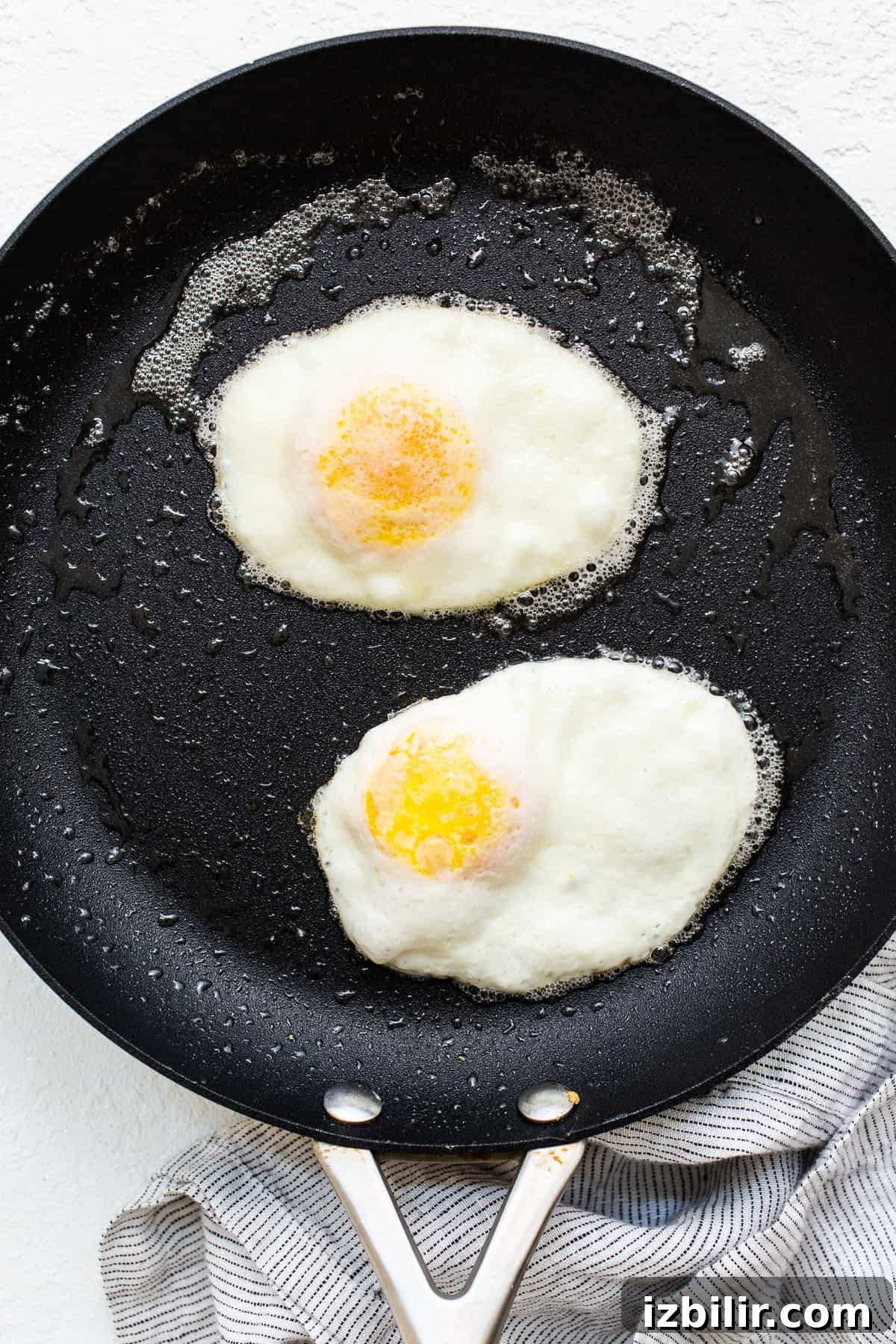 Over hard eggs cooking in a skillet with butter.