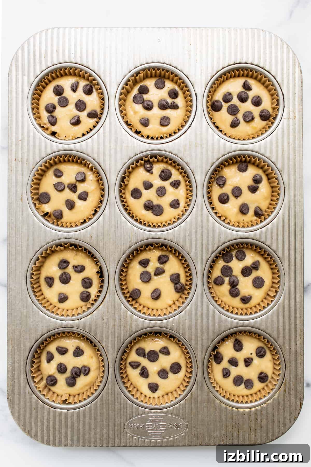 Banana bread muffin batter in muffin tins topped with chocolate chips.