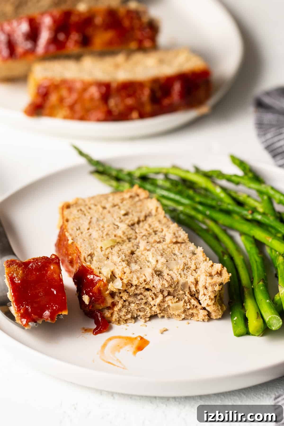 Slice of ground turkey meatloaf on a plate with asparagus.
