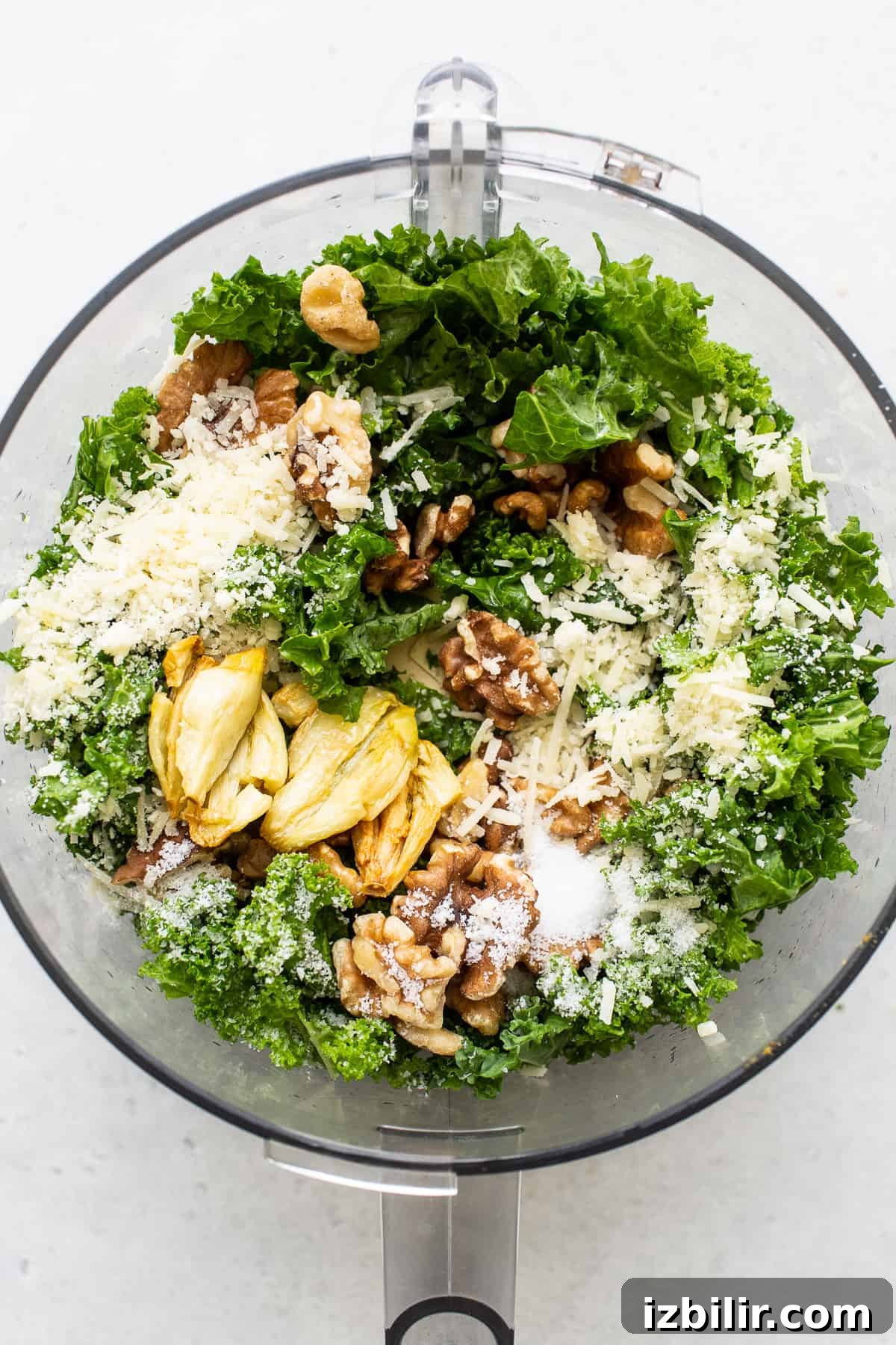 Make this easy kale pesto recipe with fresh kale, walnuts, olive oil, lemon juice, and parmesan cheese. It's the perfect complement to pasta dishes, as a dip or a marinade. All of the ingredients for kale pesto in a food processor.