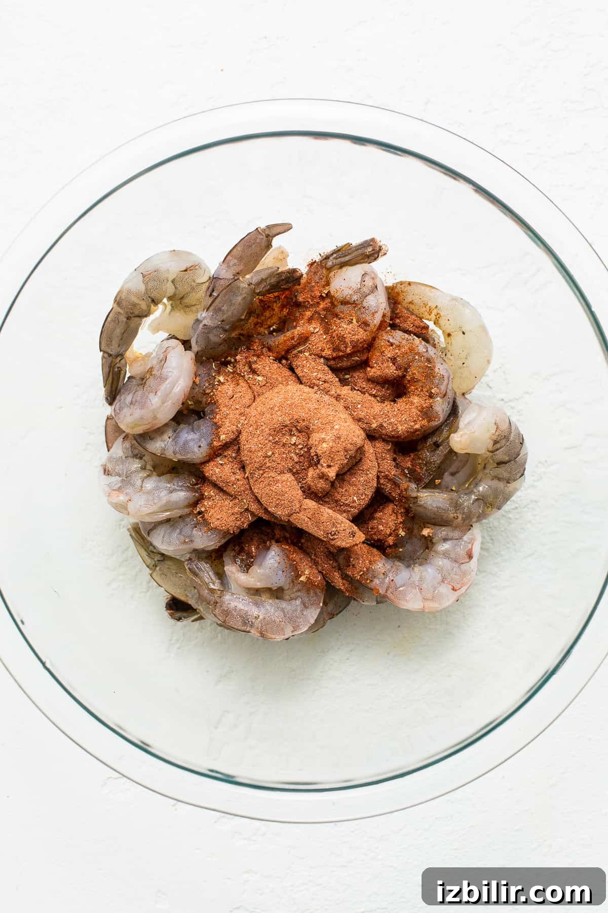 Raw shrimp in a bowl with seasoning.