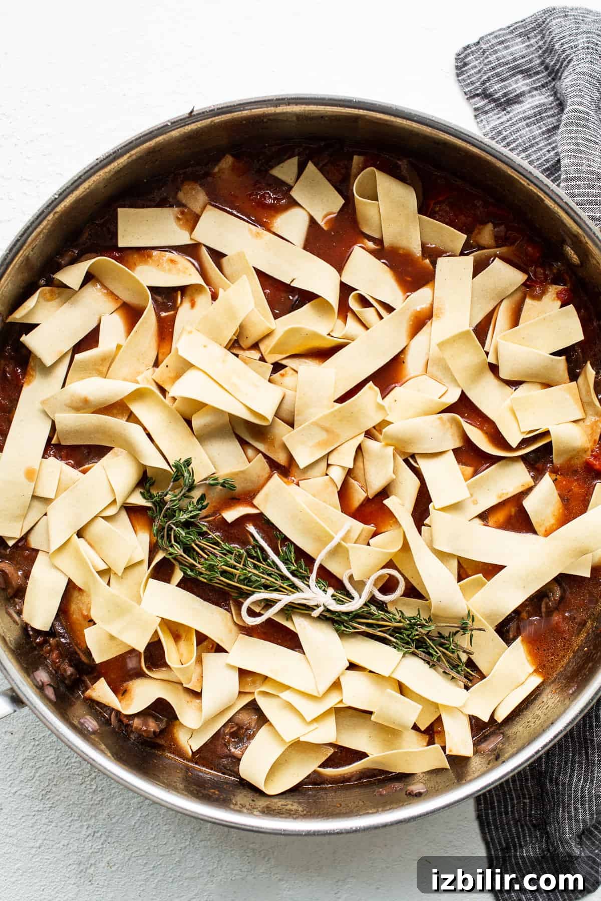 Pappardelle with sauce in skillet Pappardelle pasta over sauce in a skillet.