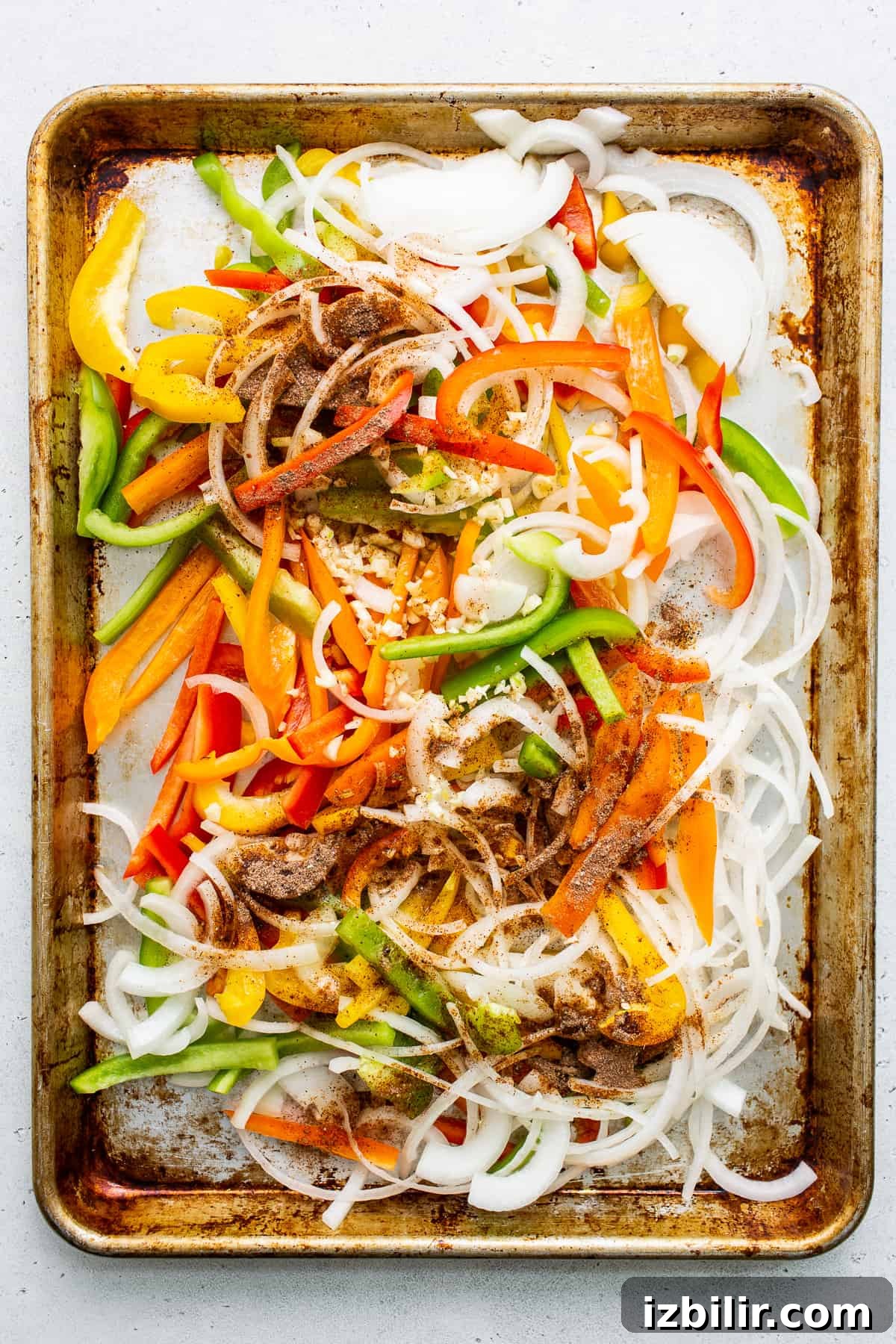 Sheet Pan Chicken Fajitas with less than 10 ingredients! This is made with chicken thighs, peppers and onions, and homemade fajita seasoning. uncooked peppers and onions on baking sheet.