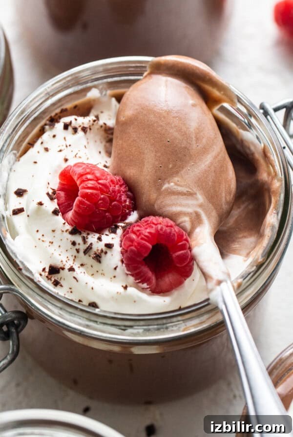 Chocolate mousse in jars with whipped cream and raspberries.