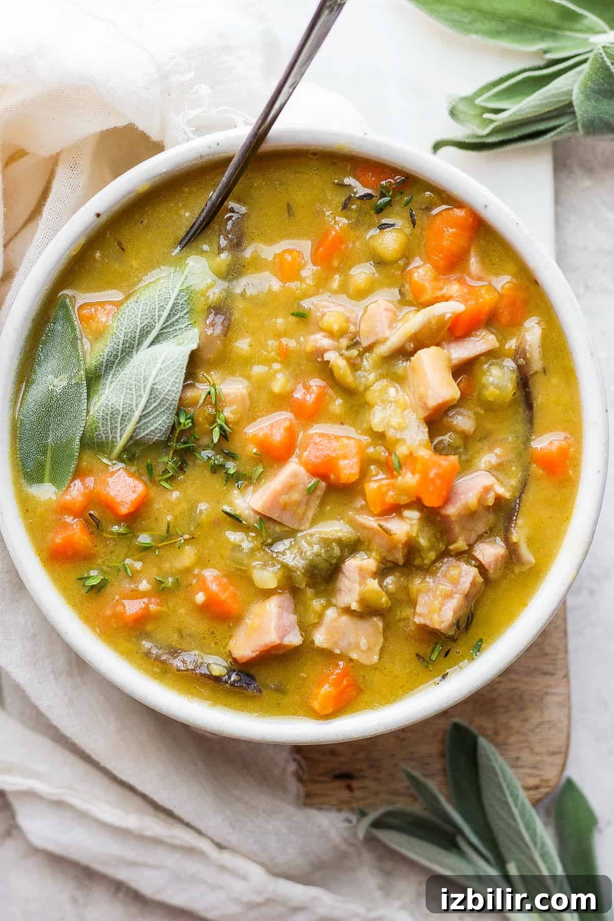 There's no better way to cozy up during the cooler months than with a warm bowl of split pea soup with ham! Smoky ham, hearty veggies starring split peas, and aromatic herbs simmer in a savory veggie broth to give you a deliciously smooth soup. Split pea soup with ham in a bowl with a spoon.