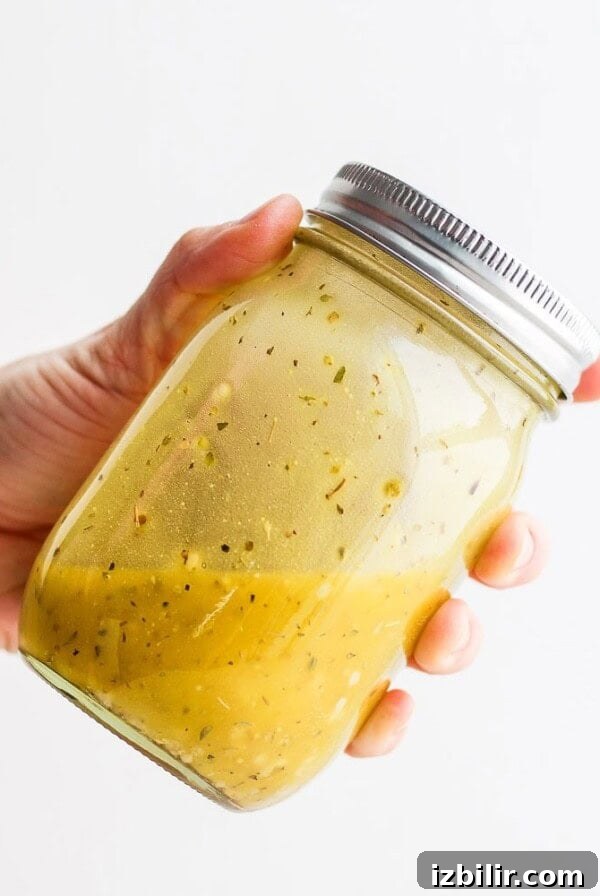 a hand holding a jar of Greek salad dressing.