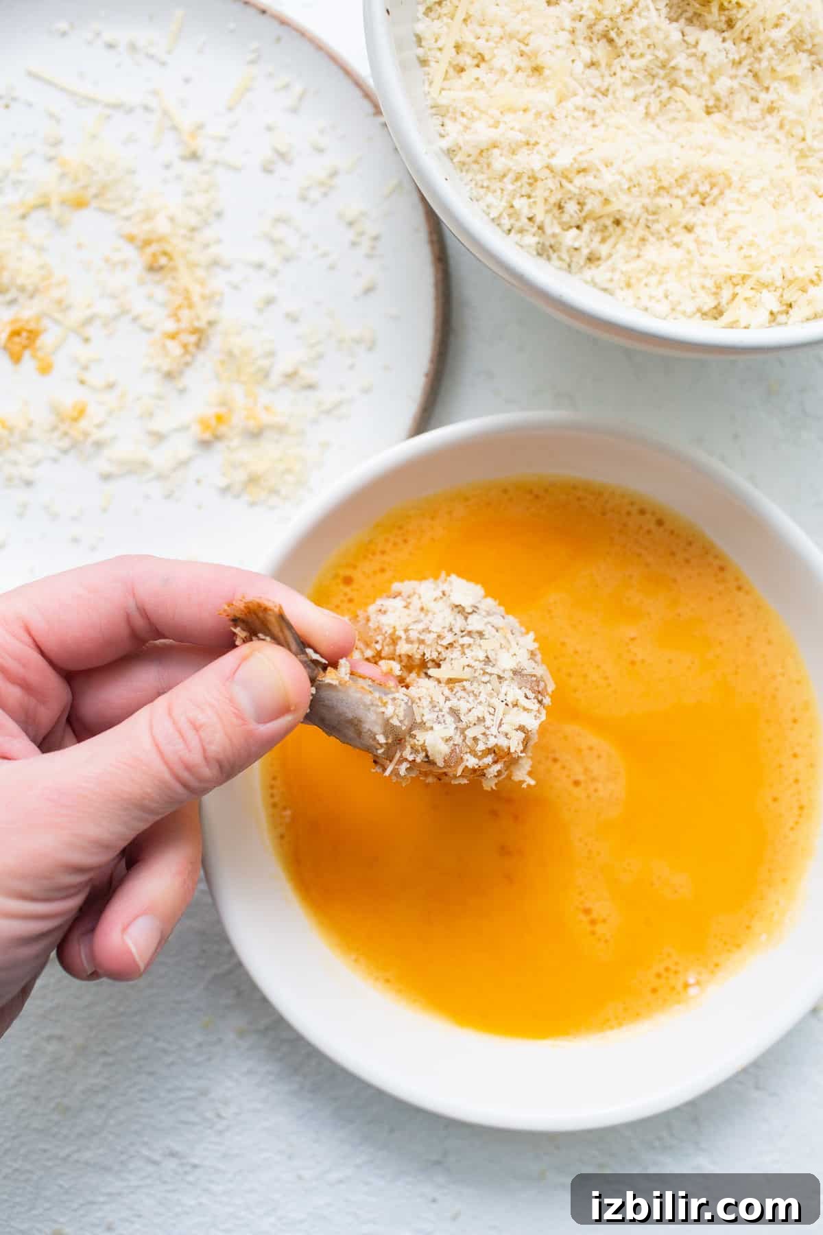 Panko coated shrimp being dipped into an egg wash.