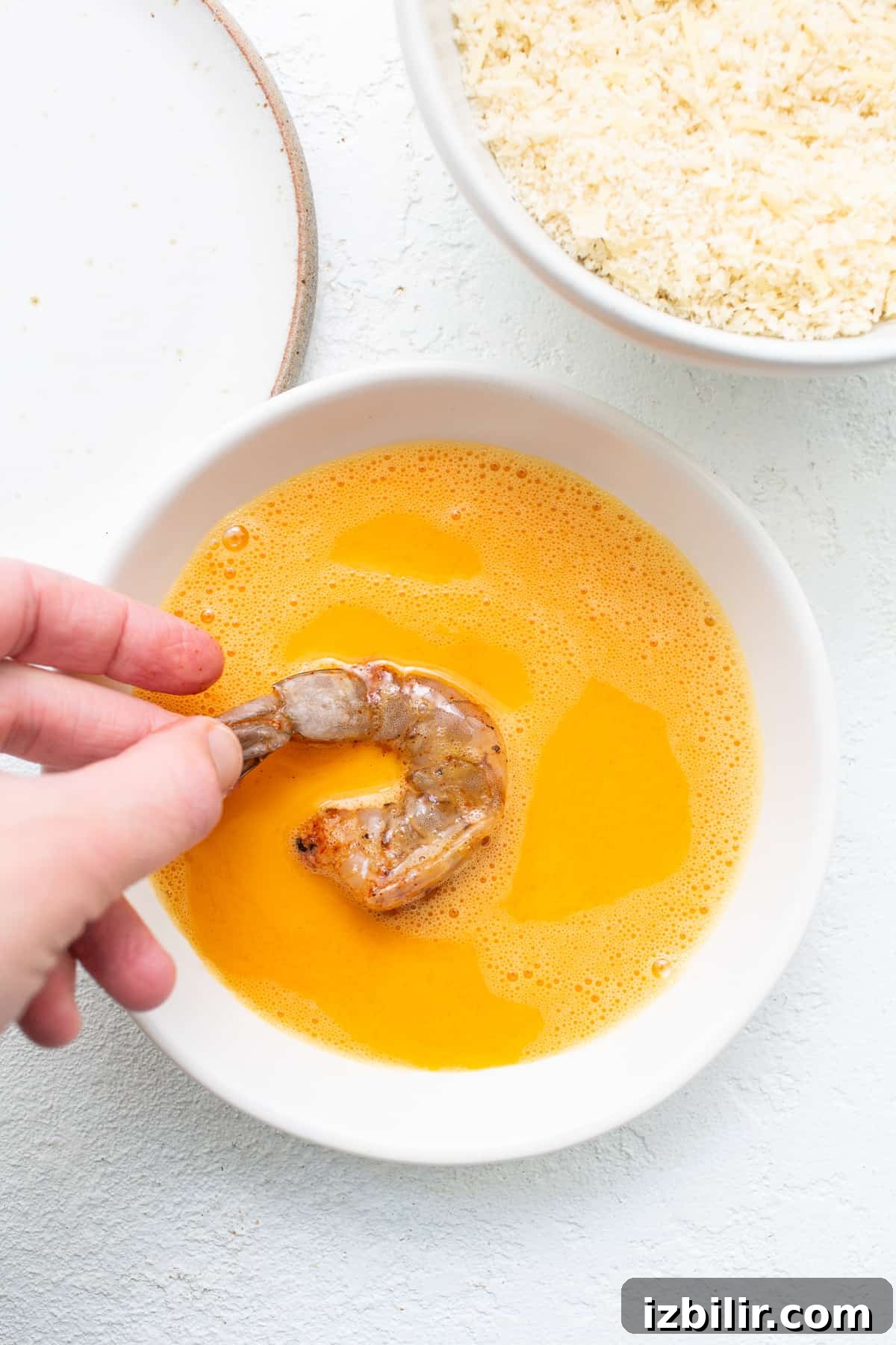 Shrimp being dipped into an egg wash.