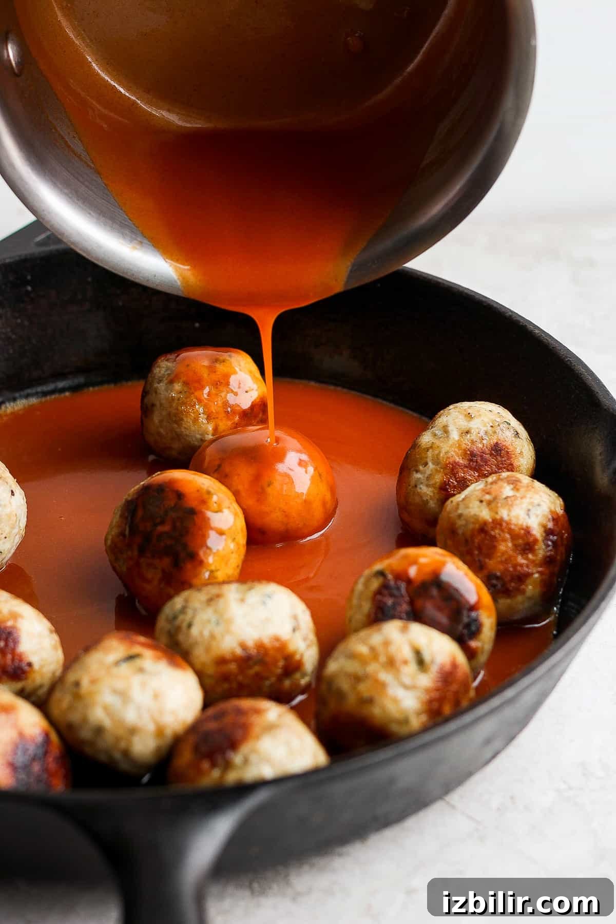 pouring buffalo sauce on top of meatballs
