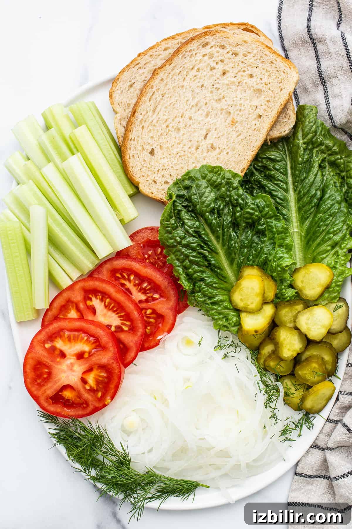 Creamy Homemade Egg Salad Sandwich 4 Lettuce, celery, pickles, tomatoes, onion, and bread on a plate.