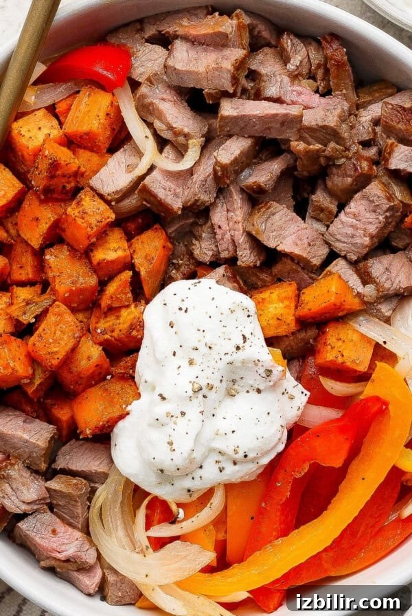 A bowl containing diced steak, roasted sweet potatoes, onions and sour cream.