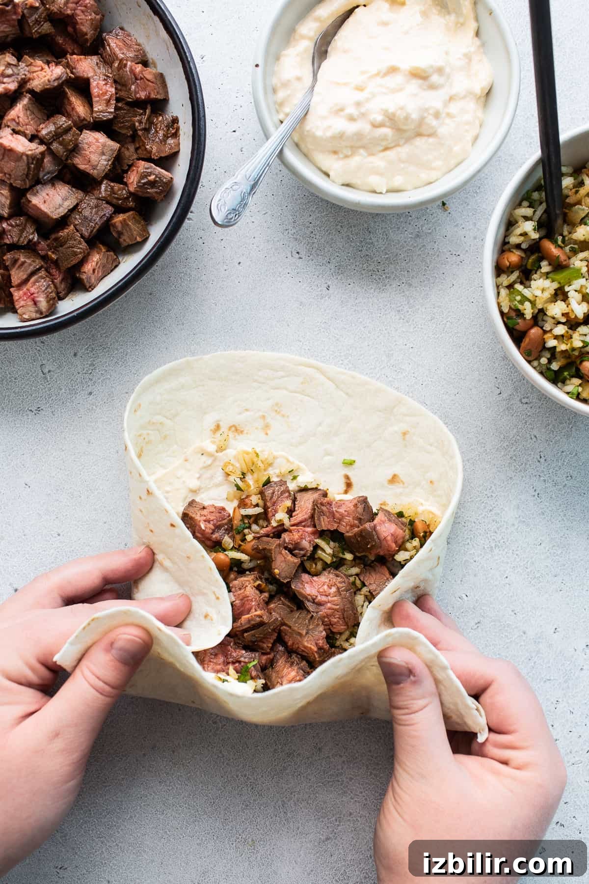 Hands rolling a steak burrito on a counter.