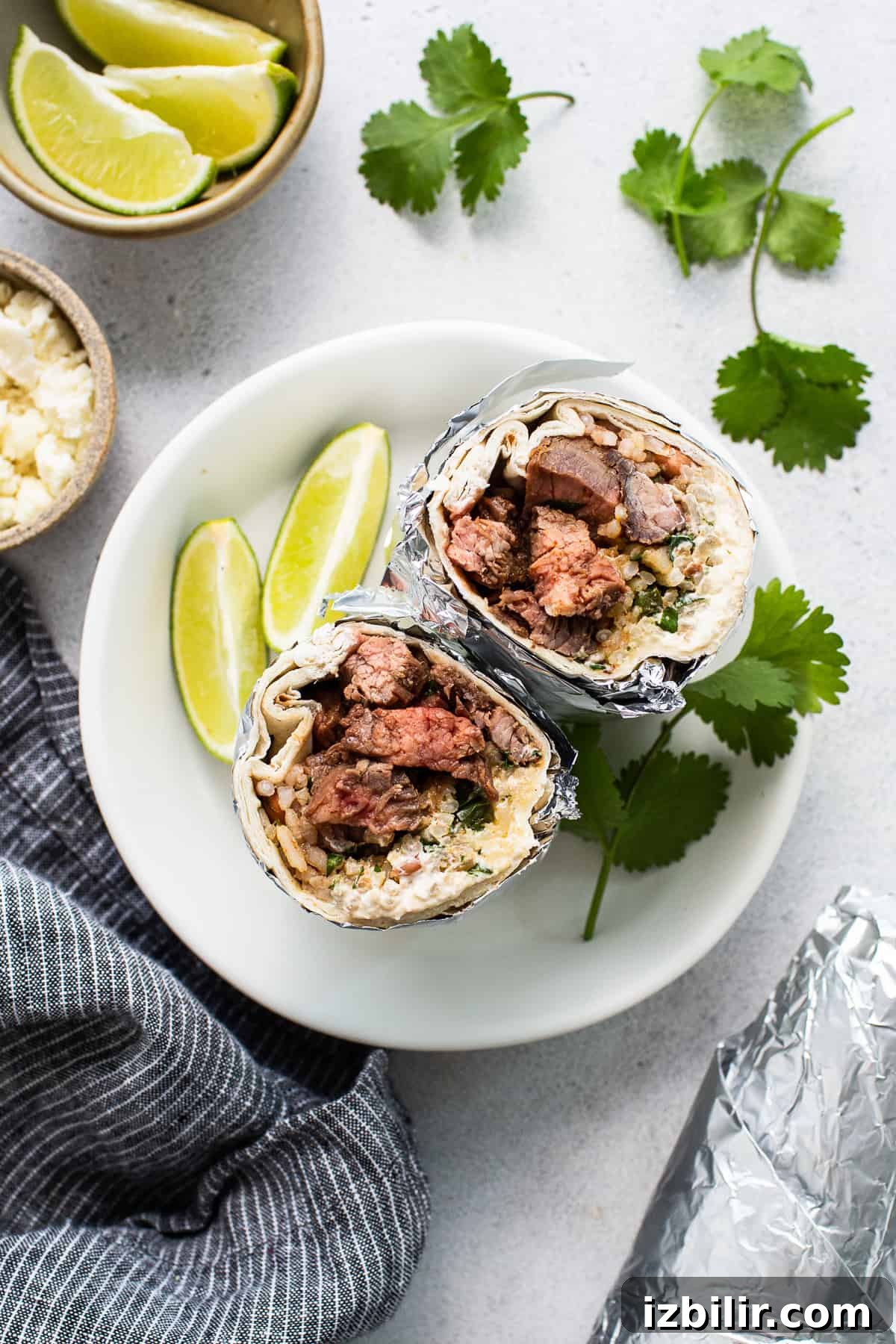 Steak burrito on a plate with sliced limes and cilantro.