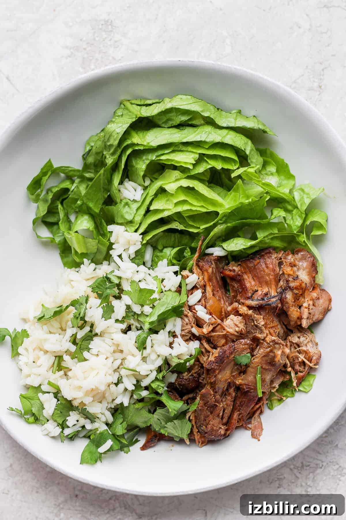 Slow Cooker Carnitas Burrito Bowls with Cilantro Lime Rice 5 A white plate with slow cooker carnitas and greens.
