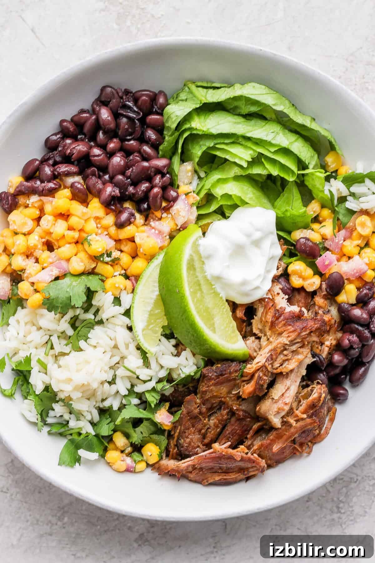 Slow Cooker Carnitas Burrito Bowls with Cilantro Lime Rice 8 A bowl of slow cooker carnitas salad with corn, beans, and sour cream