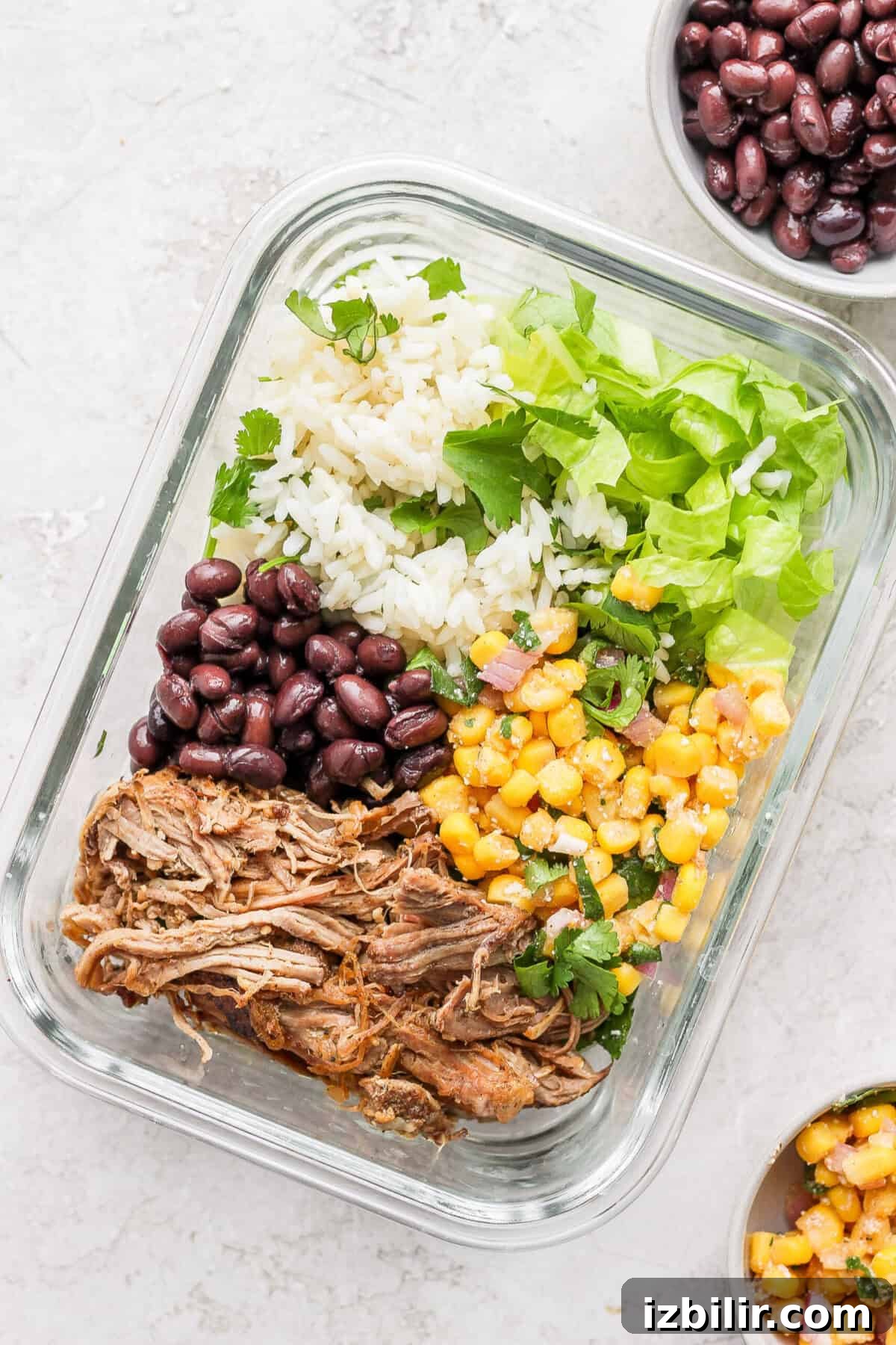 Slow Cooker Carnitas Burrito Bowls with Cilantro Lime Rice 9 A slow cooker carnitas meal with rice, beans, and corn served in a glass container.