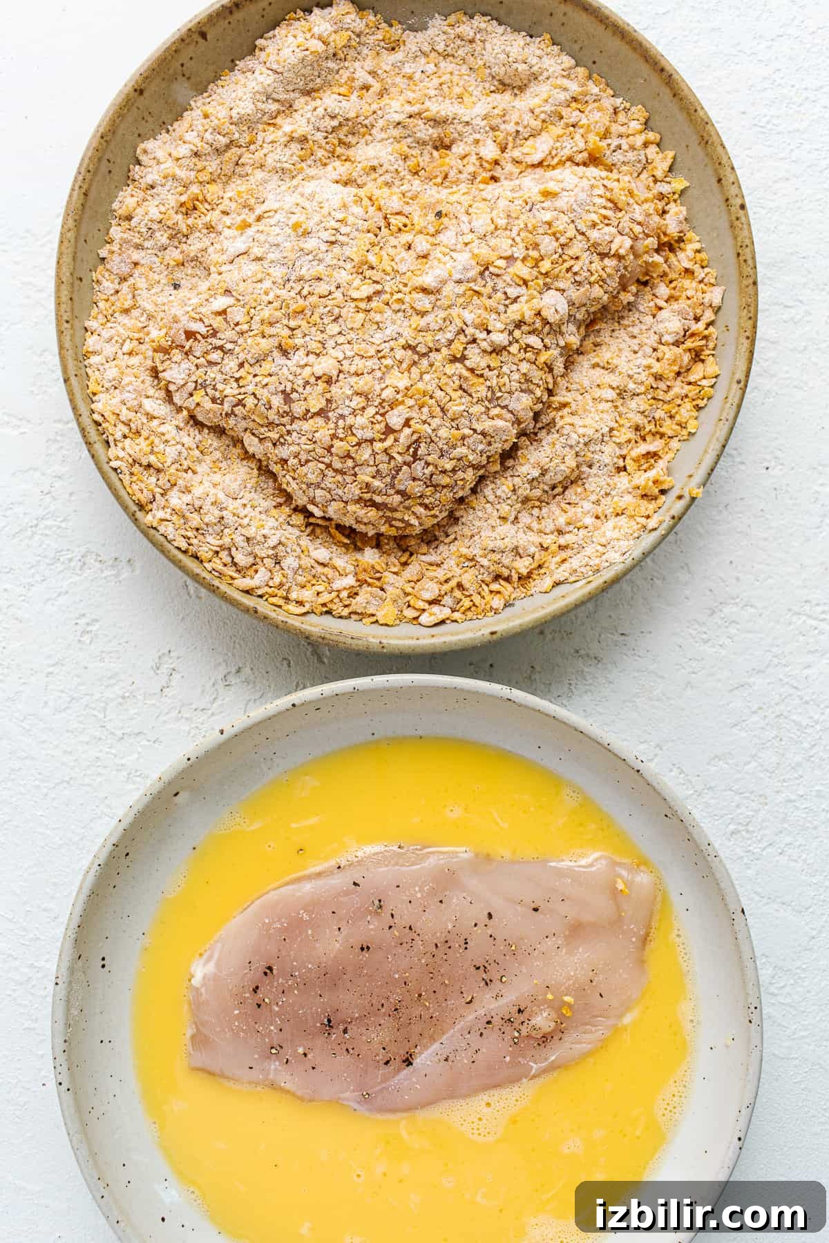 Dredging chicken breast in egg and cornflake coating Dredging chicken in egg and topping.