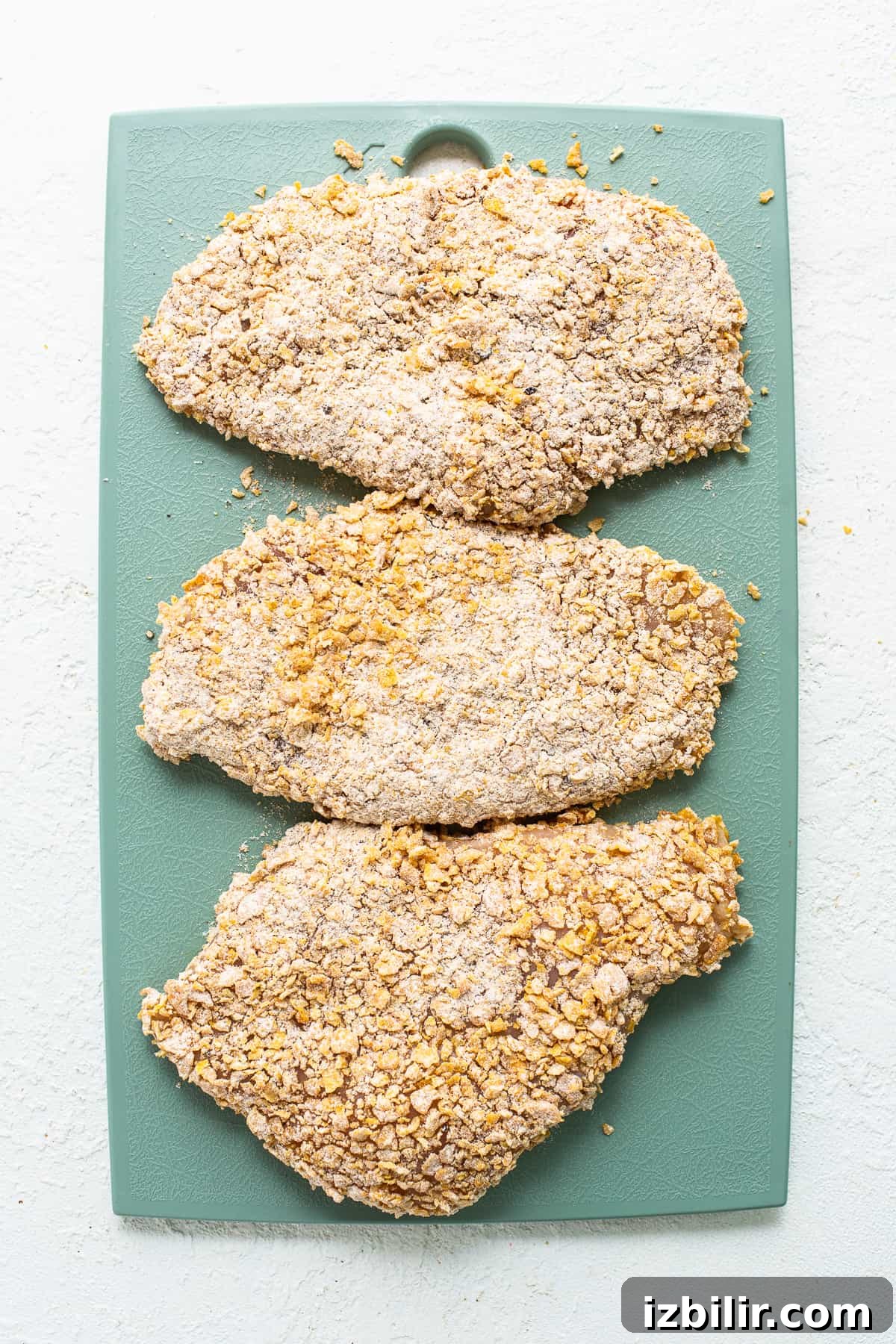 Uncooked pounded chicken breasts ready for breading Uncooked chicken on cutting board.