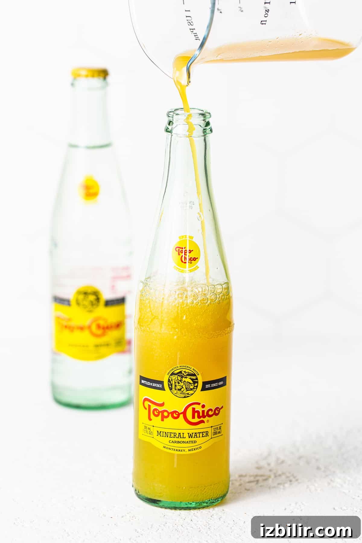 Mango juice being poured into a topo chico bottle.