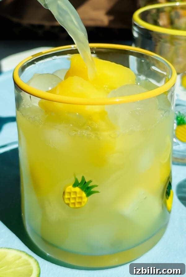 A glass decorated with small pineapples filled with yellow frozen drink.