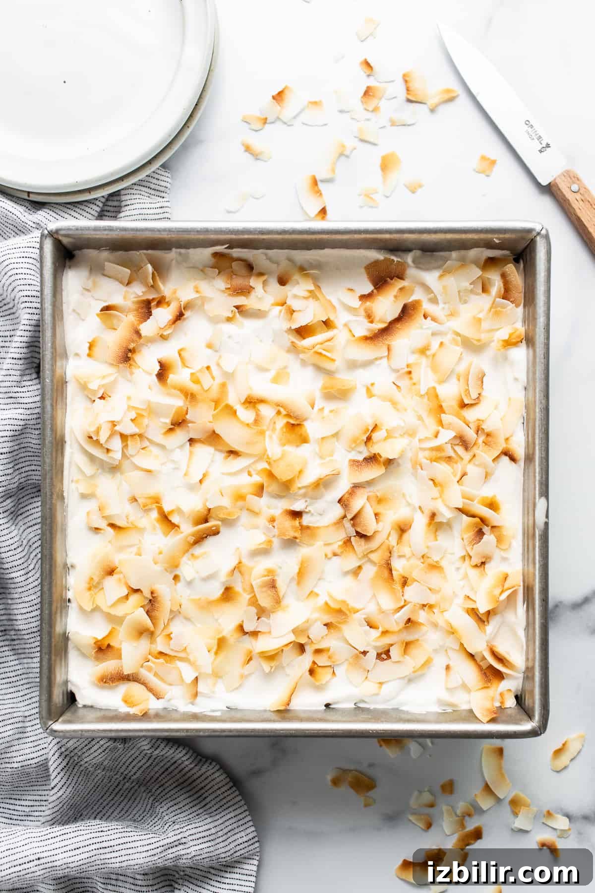 Coconut Cream Pie Bars with Toasted Coconut Topping 6 A pan filled with a dessert covered in coconut flakes.