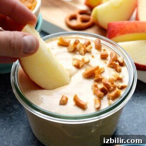Creamy Pumpkin Dip with Greek Yogurt Recipe 6 A person dipping a pretzel into a bowl of pumpkin yogurt dip.