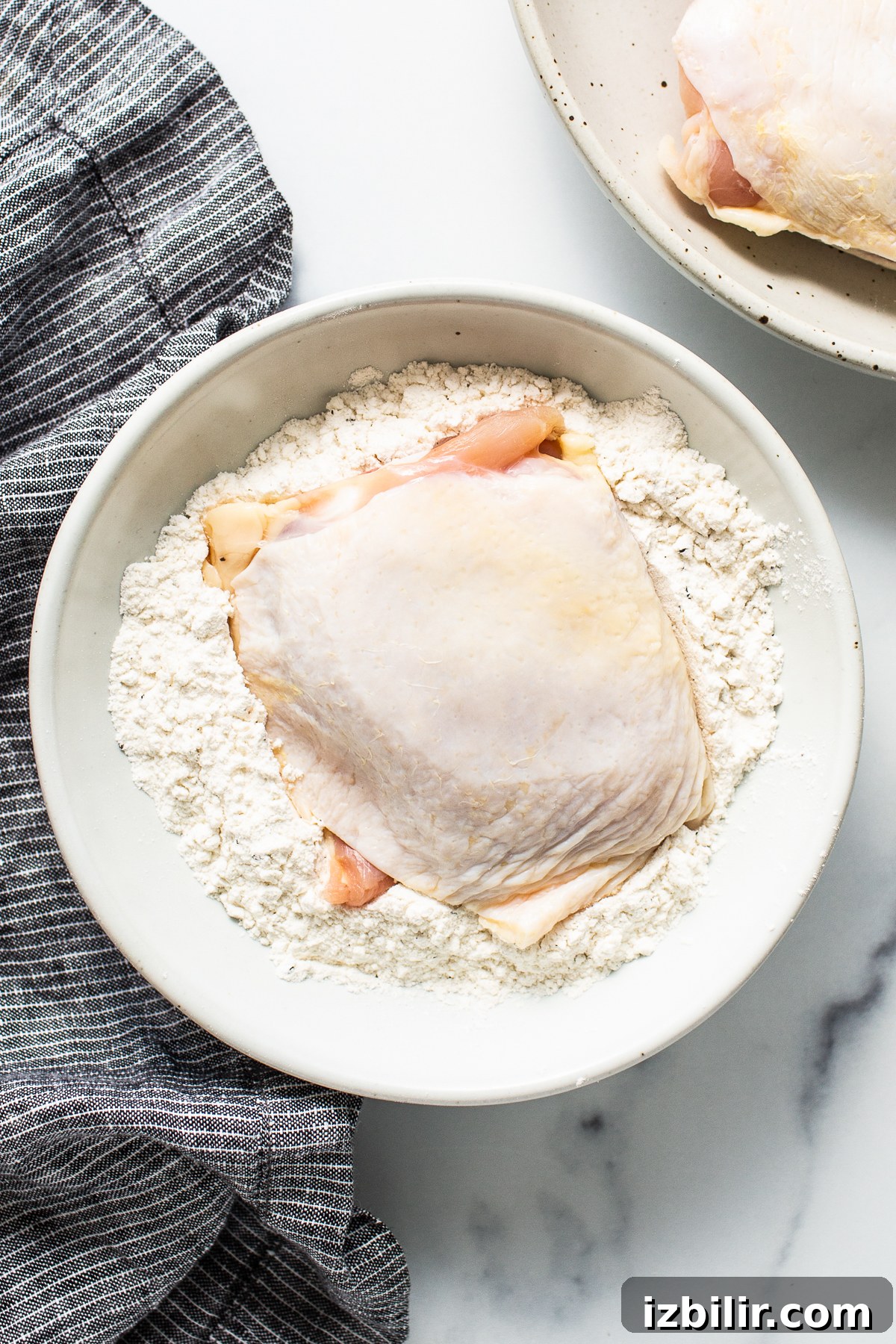 raw chicken thigh being dredged in flour.