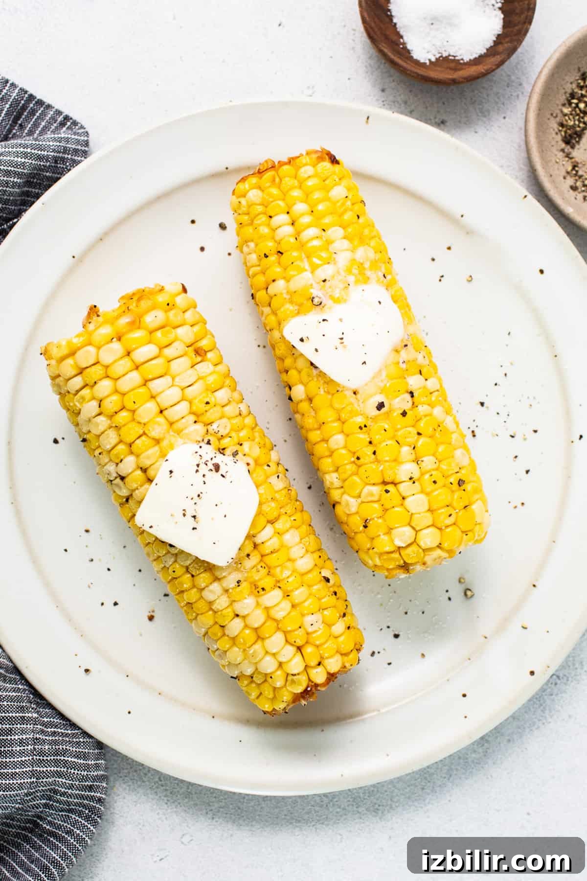 two corn on the cob with butter on top.