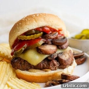 a burger with mushrooms, cheese and pickles on a plate.