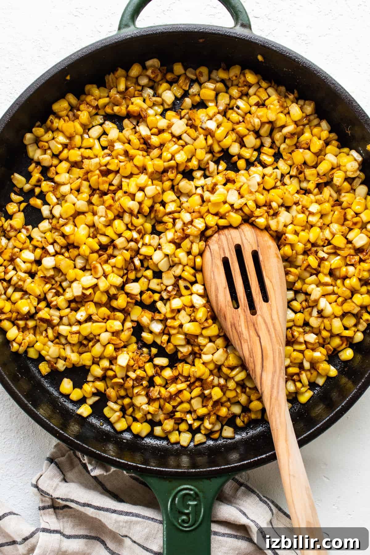 Corn in a skillet with a wooden spoon.