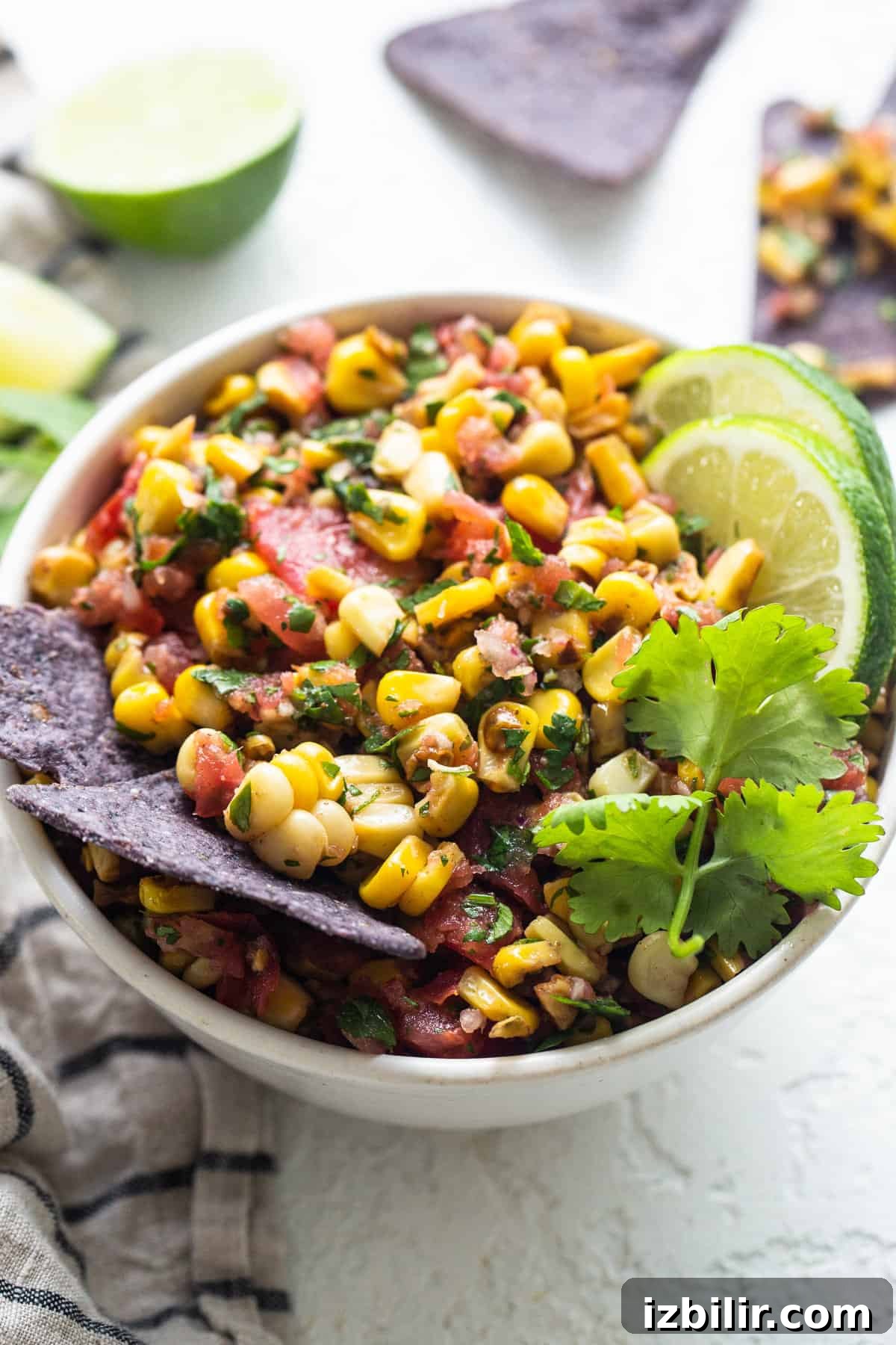 Mexican corn salsa in a white bowl with limes and tortilla chips.