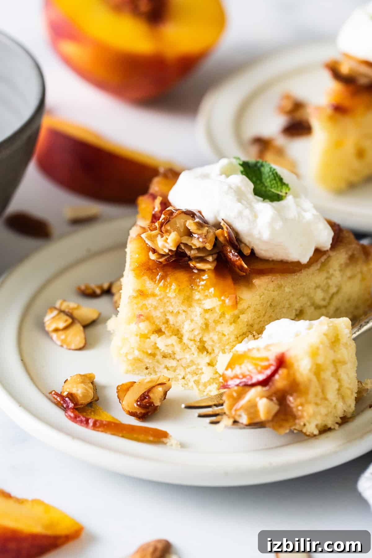 Caramelized Peach Upside Down Cake Recipe 2 A slice of peach cake with whipped cream and almonds on a plate.
