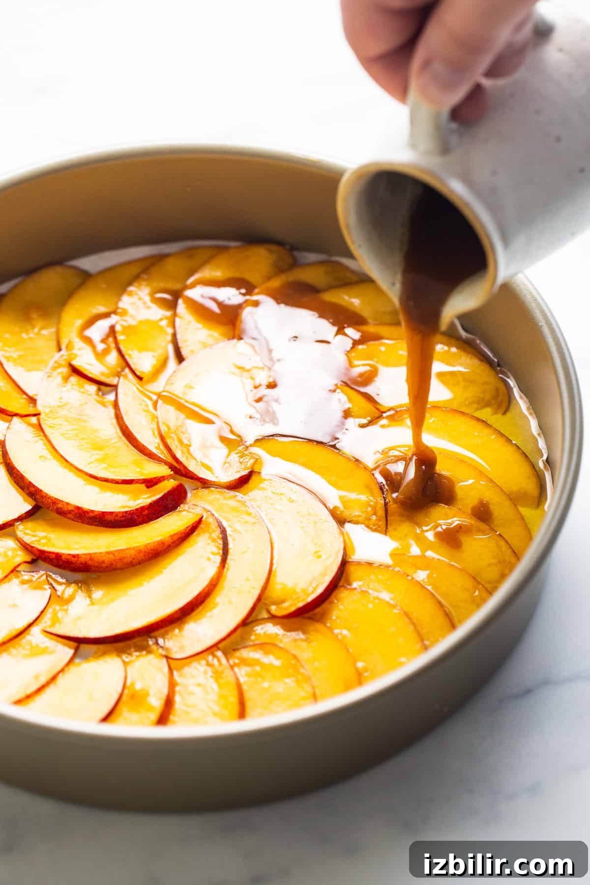 Caramelized Peach Upside Down Cake Recipe 3 A person pouring caramel over a peach tart in a pan.