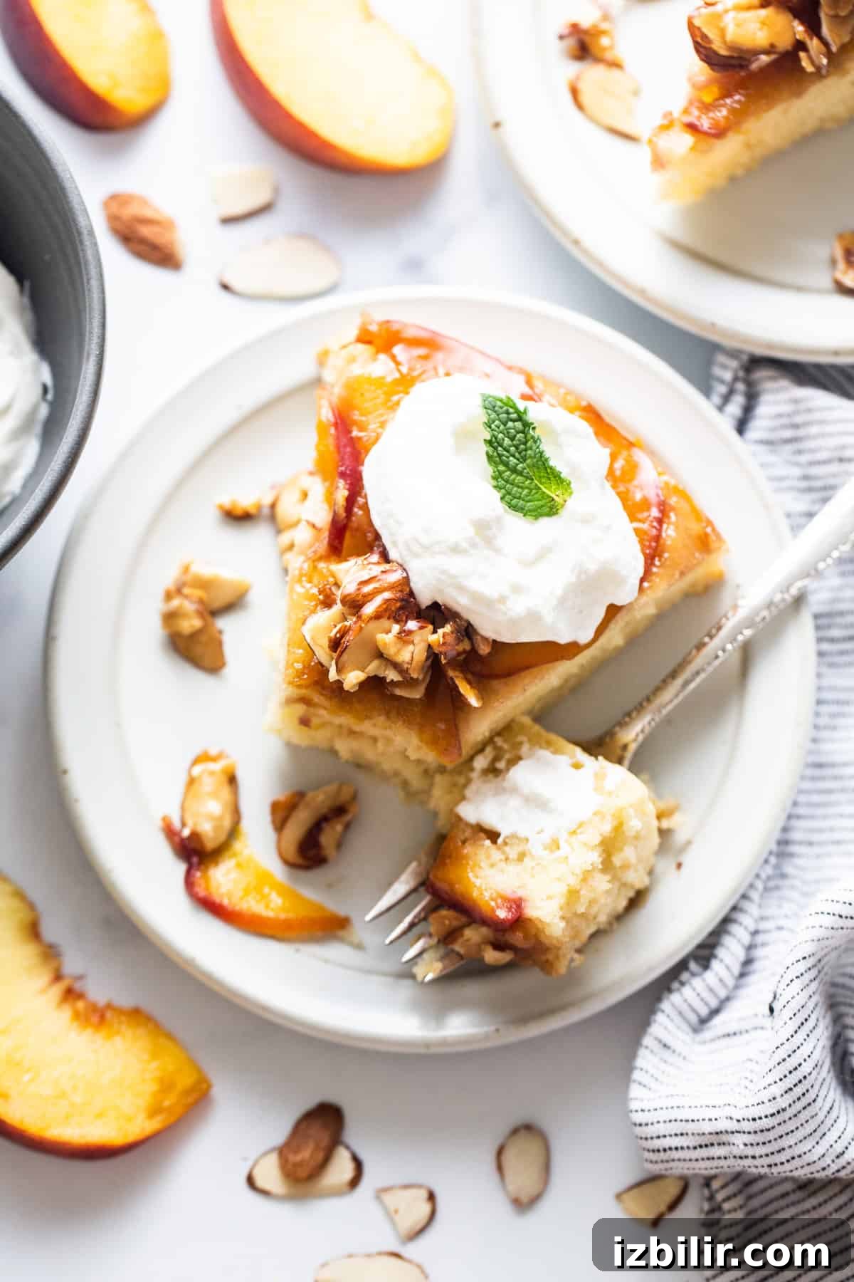 Caramelized Peach Upside Down Cake Recipe 7 A slice of peach cake with whipped cream and almonds on a plate.