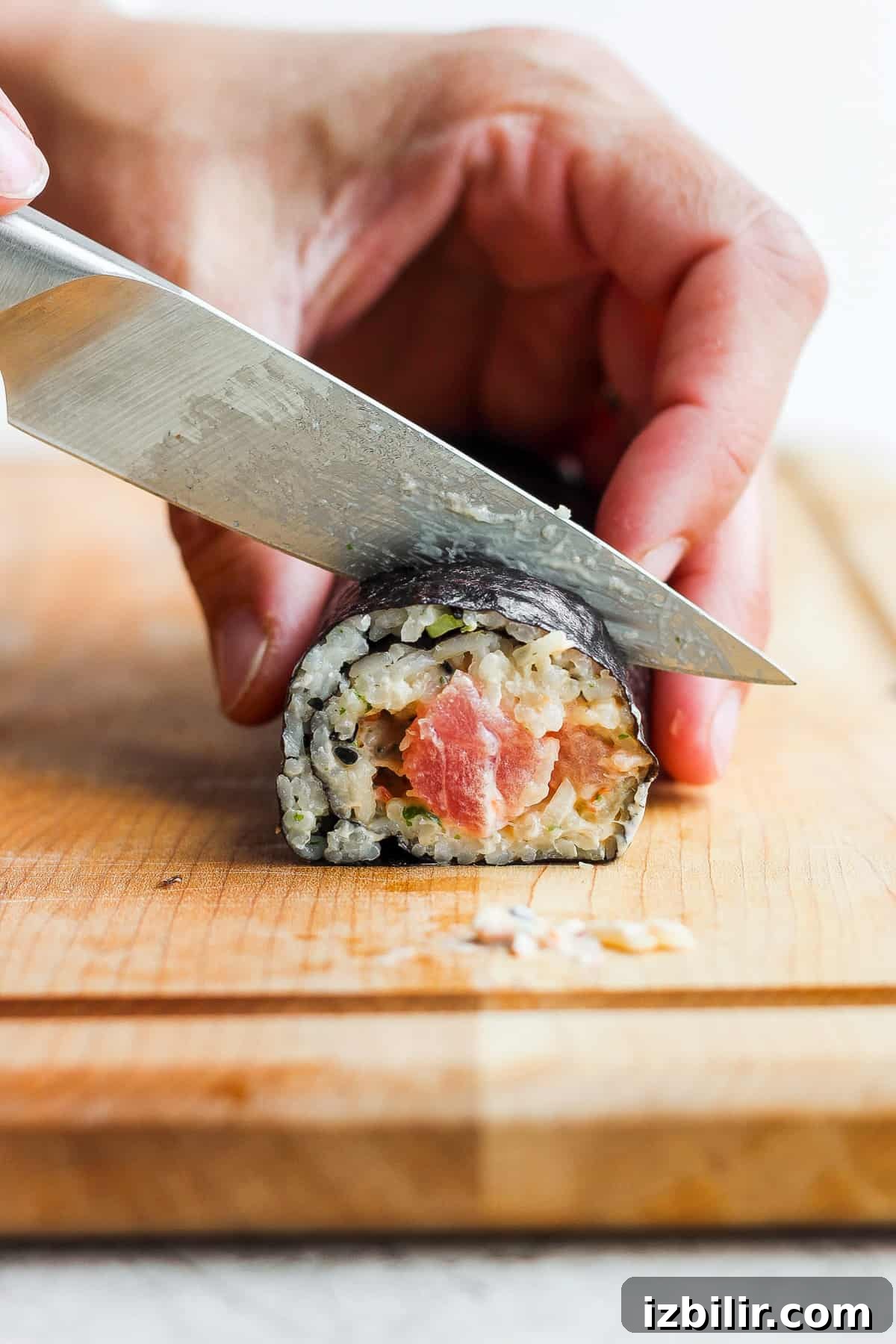 Spicy Tuna Roll Recipe: How to Make at Home 9 a person cutting sushi with a knife on a cutting board.