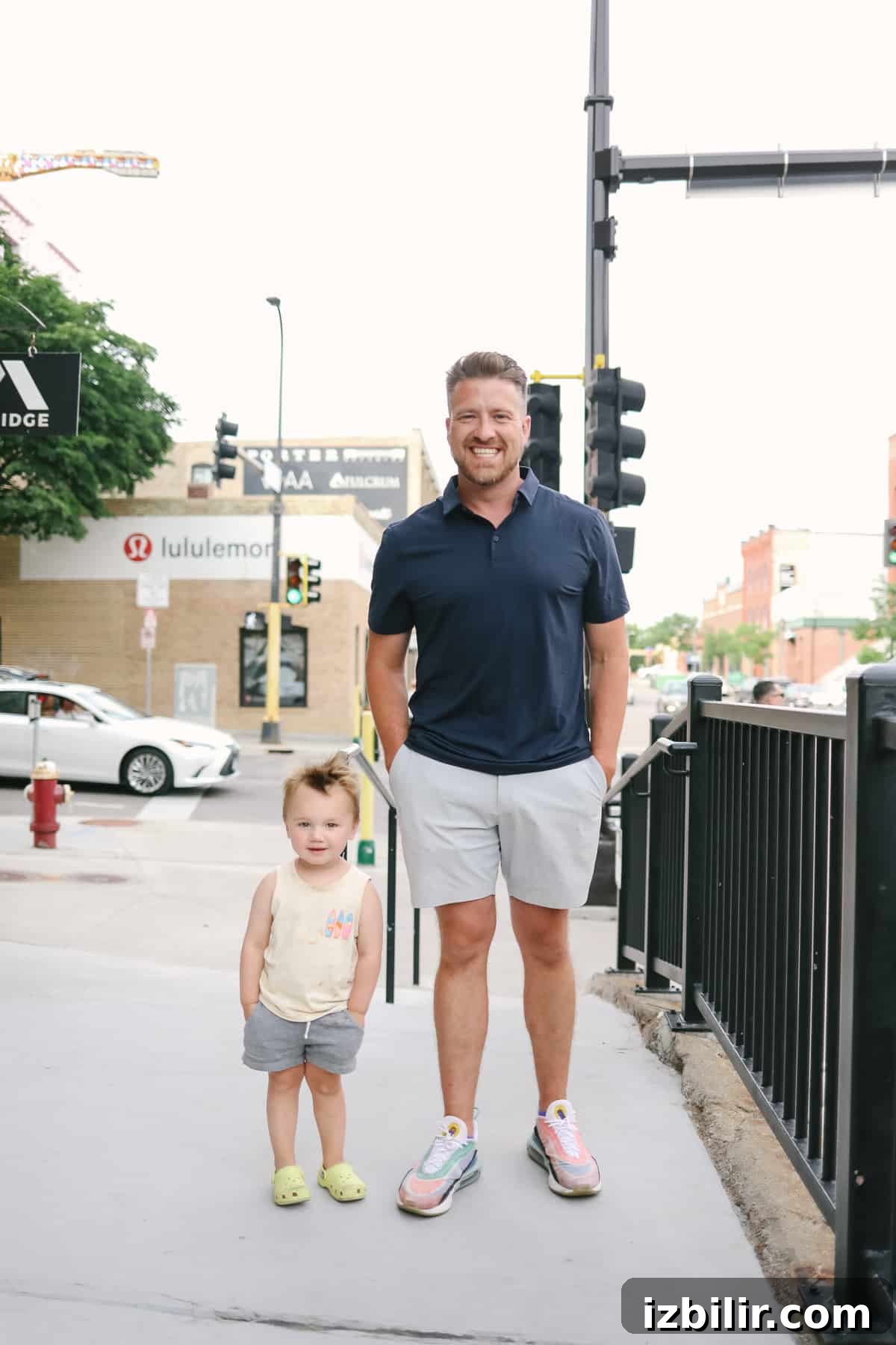 Dad standing with young child on a sidewalk, wearing casual shorts.