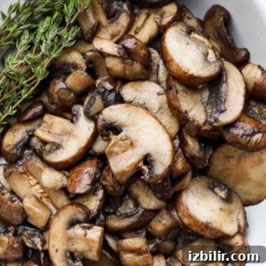 Grilled Mushroom Swiss Burger Recipe 7 roasted mushrooms in a white bowl with a sprig of thyme.